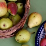 A vibrant assortment of pears and apples in a woven basket and ceramic plate, showcasing freshness.